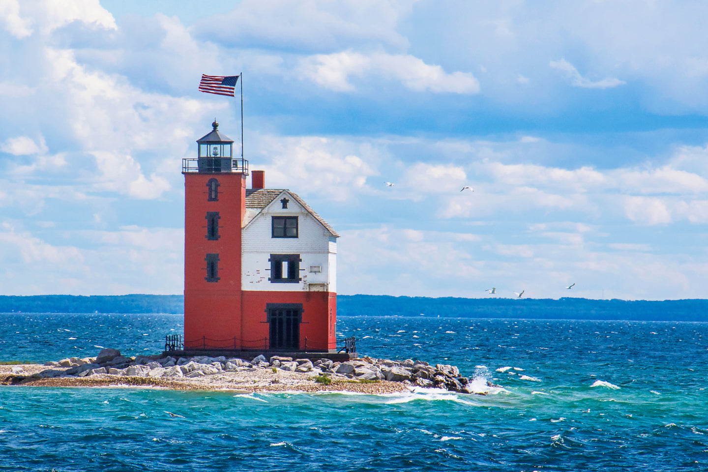 The USA flag flies over Round Island Lighthouse across the channel from Mackinac Island. The lighthouse serves as the finish line for sailing races starting from Chicago and Bayview Yacht Clubs each summer.