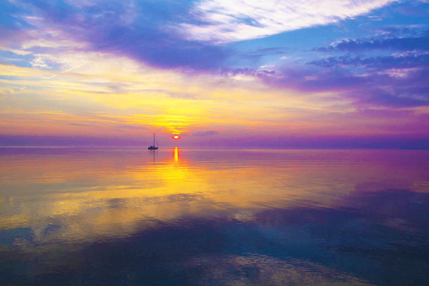 A view of the sunrise and a silhouette of a sail boat on the horizon from the shore of Round Island in the Straits of Mackinac by Jennifer Wohletz of Mackinac Island.
